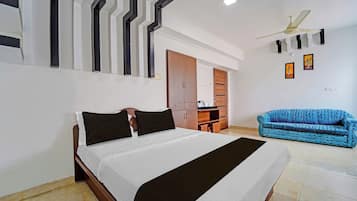 A hotel room with a bed, a blue sofa, a ceiling fan, and a wall with a geometric pattern.