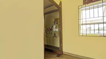A hallway with a door leading to a room, a window with a metal grid, and a wall with a poster.