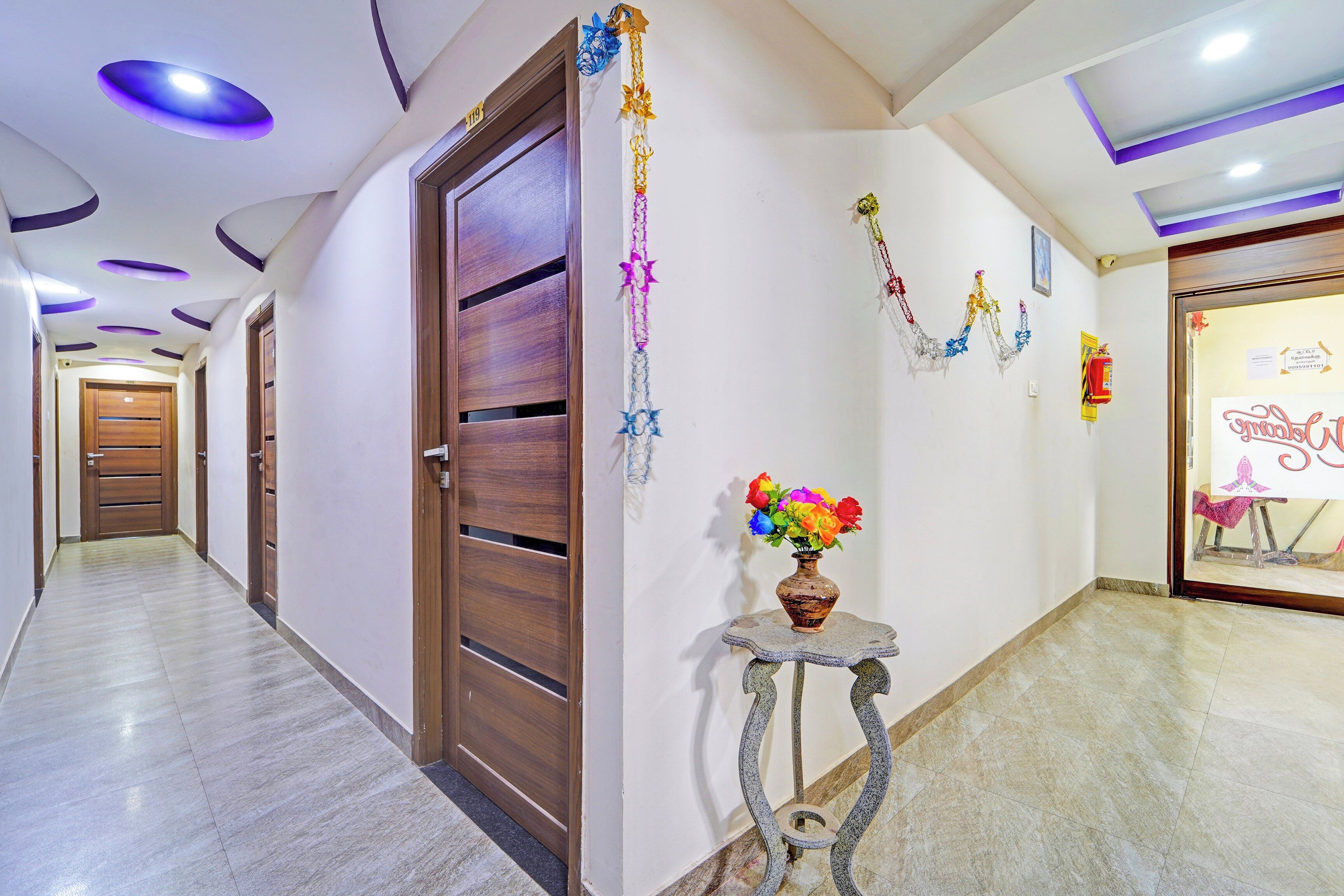 Ein Korridor mit einer Holztür, einem kleinen Tisch mit Blumen in einer Vase und einer Wand mit dekorativen Elementen.