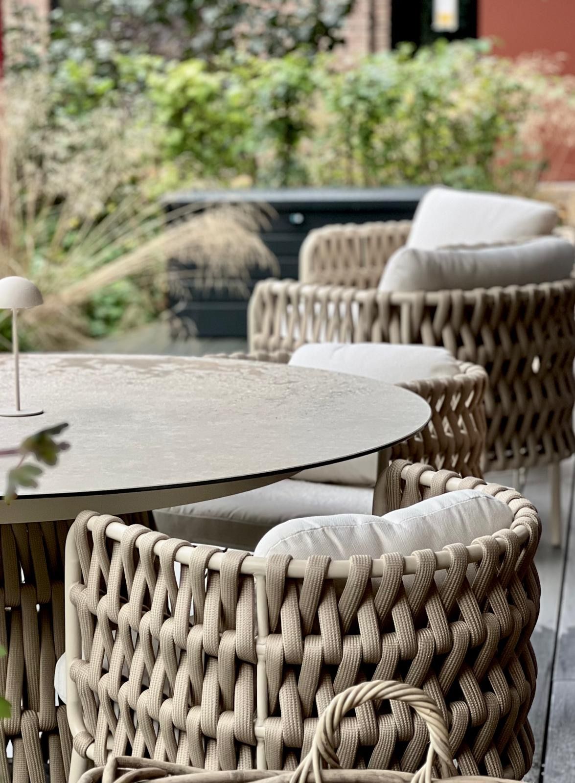 A wicker outdoor seating area with a round table and cushioned chairs.