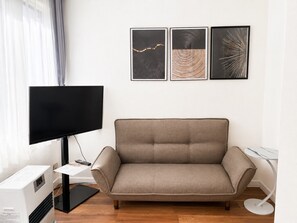 A living room with a flat-screen TV, a sofa, and three framed artworks on the wall. - New Listing (小樽市)