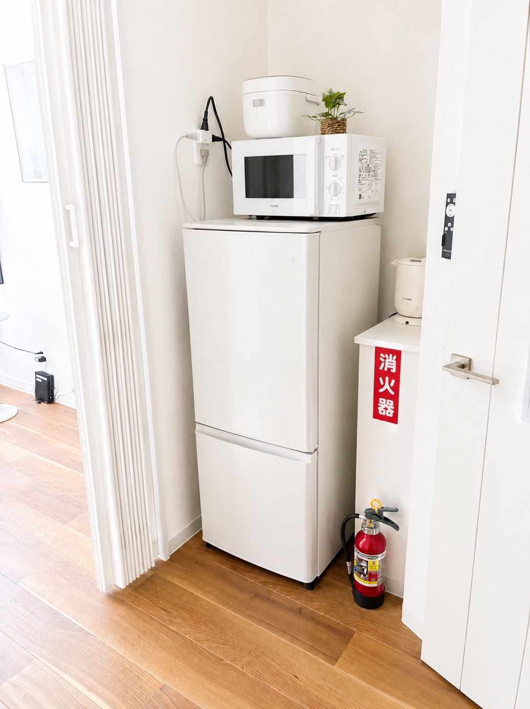 A compact kitchenette with a white refrigerator, microwave, and a small stove on top. There's a fire extinguisher on the floor beside the stove.