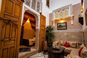 A traditional Moroccan interior with wooden doors, a bed, a sofa, and a wall-mounted shelf.
