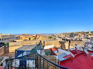 A cityscape with a prominent red-roofed building in the foreground, a clear blue sky, and a distant view of a hill with a church. - House Ismaël Luxrious Fez (Fez)