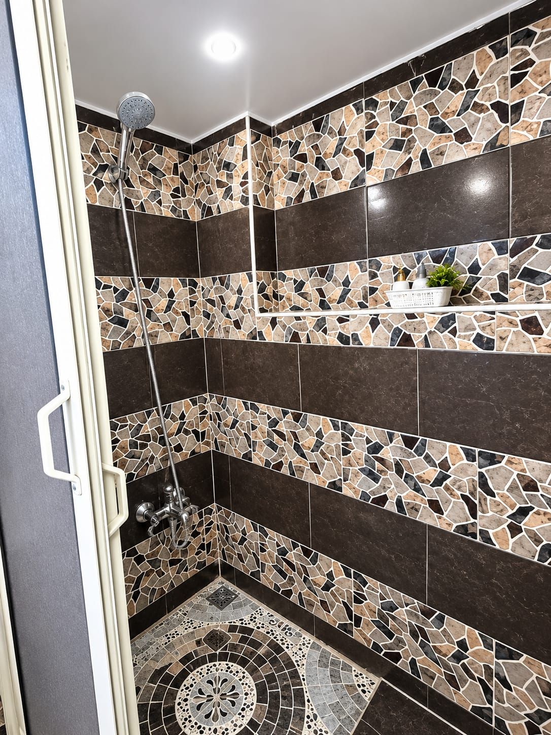 Een douche met regenstortdouche, een muur met mozaïektegelpatronen en een klein plankje met toiletartikelen.