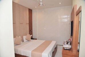 A hotel room with a bed, wooden headboard, a ceiling fan, a TV, and a bedside table with a remote control. - Hotel Ocean Borivali (Mumbai)