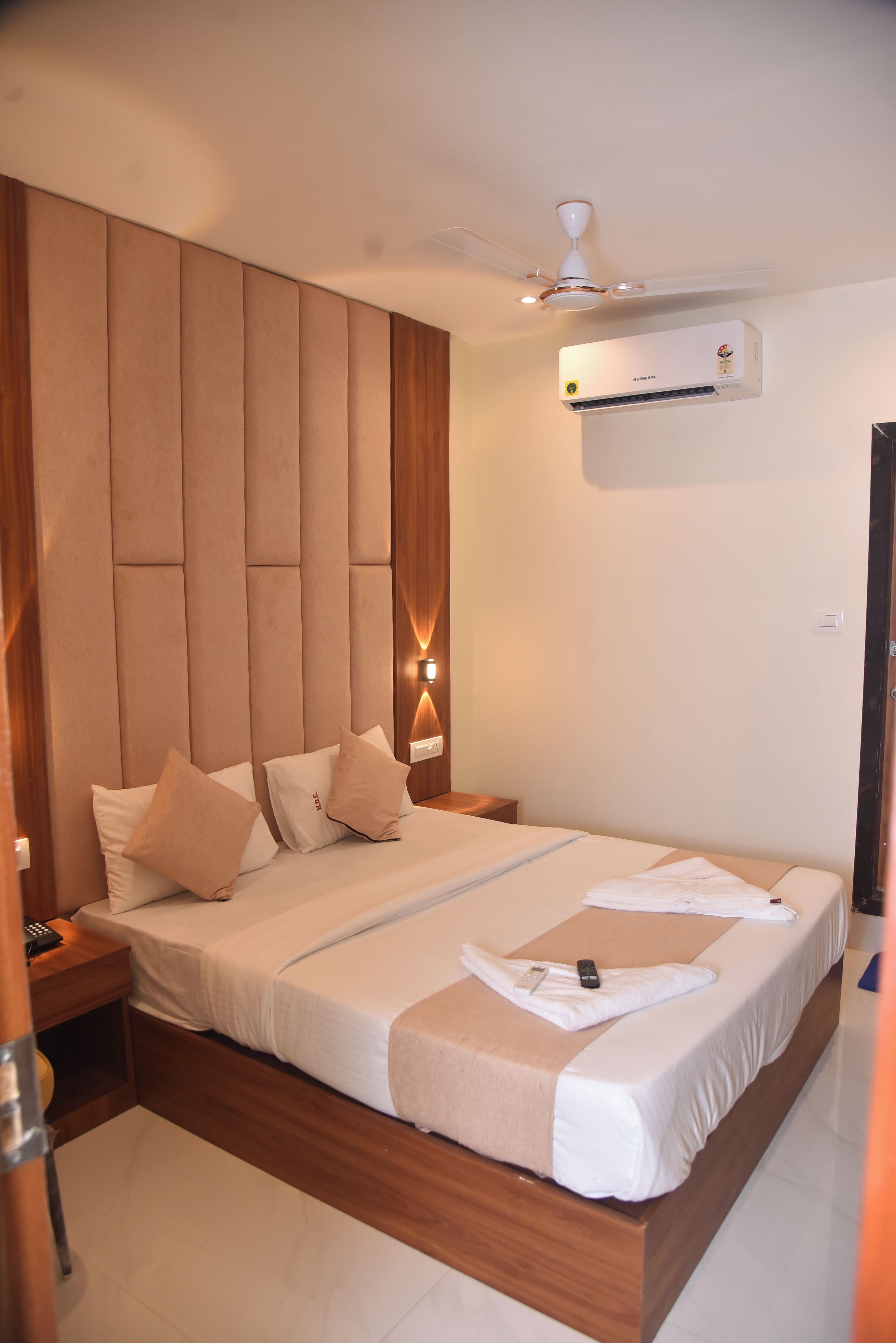Una habitación de hotel moderna con una cama grande, cabecero de madera, lámparas de noche y un equipo de aire acondicionado.
