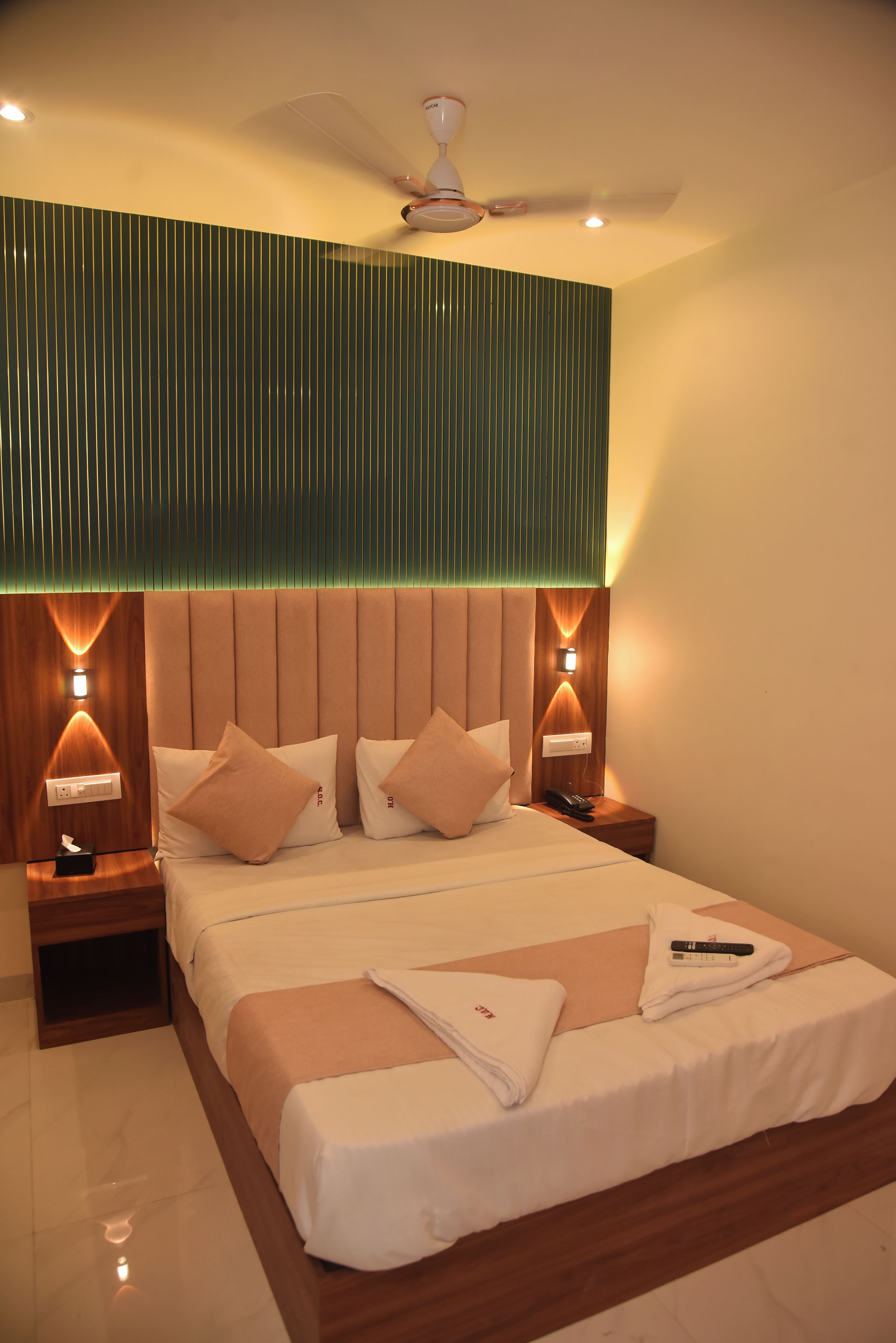 Una habitación de hotel con cama, mesitas de noche, ventilador de techo e iluminación en la pared.