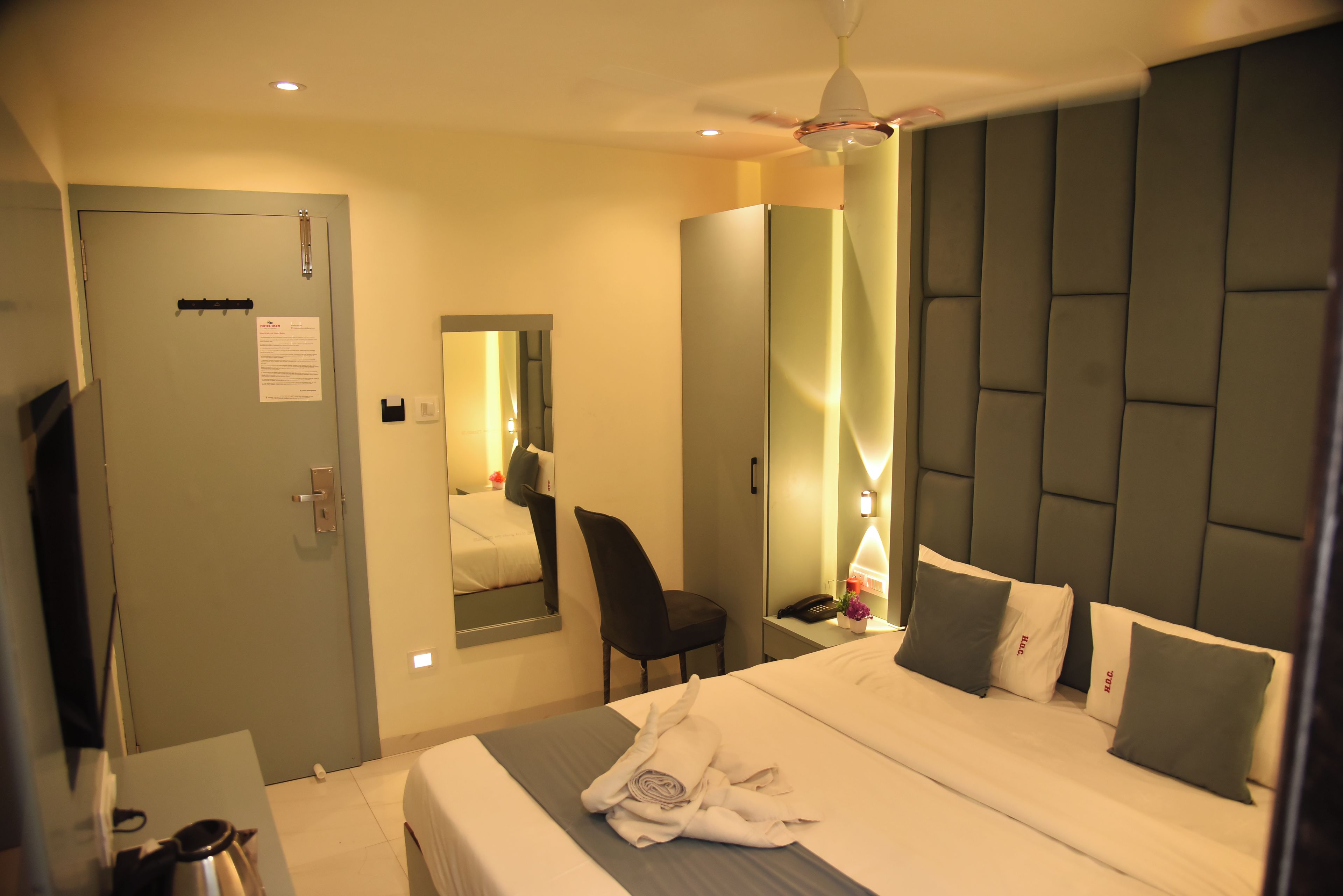 Ein Hotelzimmer mit Bett, Schreibtisch, Stuhl, Spiegel und Deckenventilator.