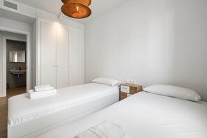 A minimalist bedroom with two beds, a nightstand, a mirror, and a bathroom visible in the background. - RDR591 - Modern 2 Bedroom Apartment in Estepona (Estepona)