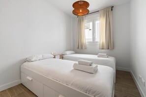Ett hotellrum med två sängar, ett nattduksbord i trä, ett fönster med gardiner och en flätad lampa.