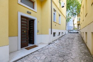 A narrow cobblestone street flanked by yellow buildings with a wooden door and a small window. - GuestHost - Ondina Apartment in Downtown Pesaro (Pesaro)
