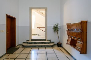 A hallway with a wooden door, a staircase leading to an upper floor, a potted plant, and a wall-mounted wooden shelf unit. - GuestHost - Ondina Apartment in Downtown Pesaro (Pesaro)