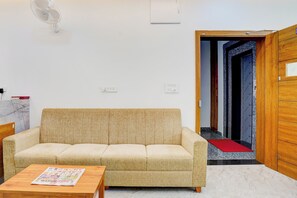 A living room with a sofa, a coffee table, a wall-mounted fan, and a door leading to another room. - Hotel O AYODHYA RESIDENCY (Bangalore)