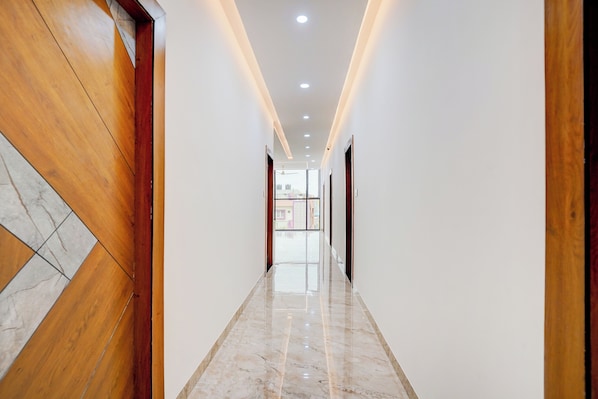 Un pasillo con puerta de madera a la izquierda, piso de mármol e iluminación empotrada.