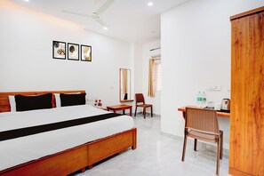 A hotel room with a bed, a desk, a chair, a wardrobe, and a ceiling fan. - Hotel O AYODHYA RESIDENCY (Bangalore)