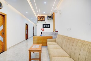 A reception area with a sofa, a wooden table, a reception desk, and a wall-mounted sign. - Hotel O AYODHYA RESIDENCY (Bangalore)