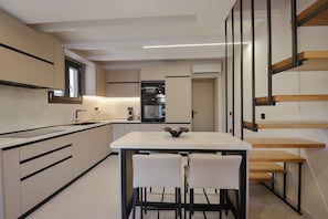A modern kitchen with a central island, built-in appliances, and a dining area with a bench and chairs. - Casa Cotsela by CorfuEscapes (Corfu)