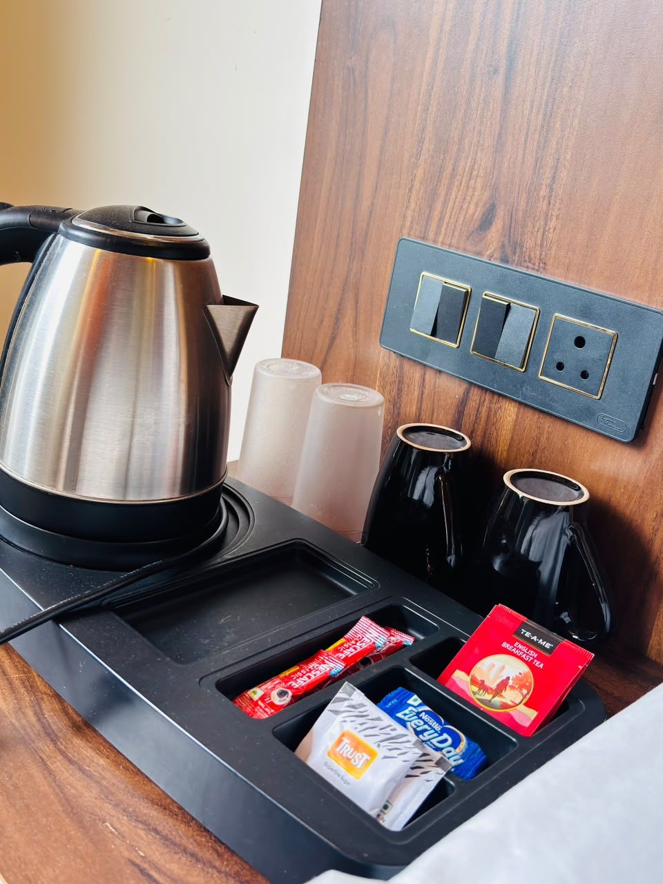 Une chambre d’hôtel équipée d’une machine à café, de sachets de thé et d’une prise électrique au mur.