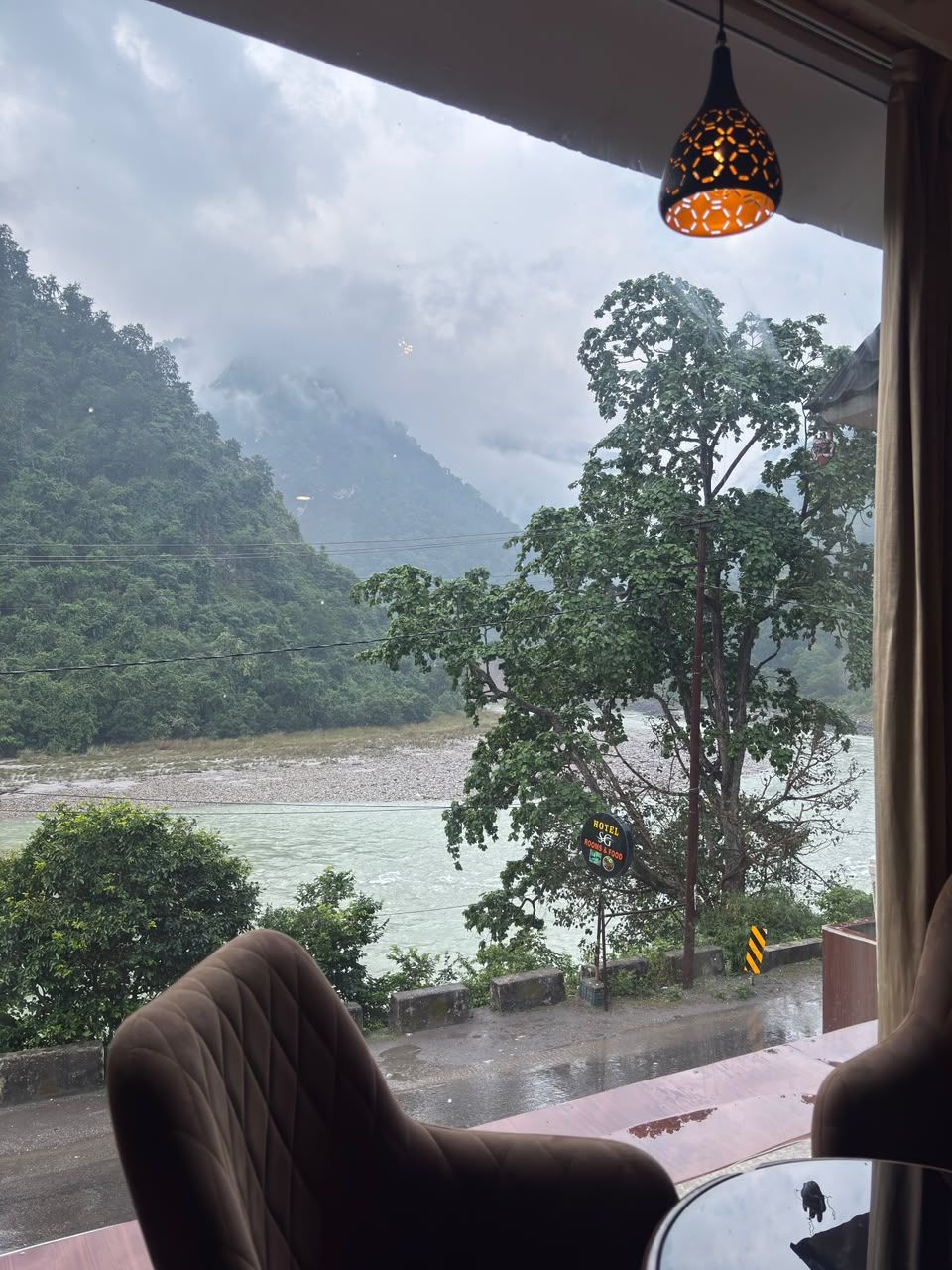 Une pièce avec vue sur une rivière et des montagnes, une lampe suspendue et une table.