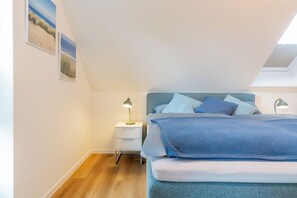 A bedroom with a bed, a nightstand, a lamp, and two wall-mounted pictures. - Wind Force 7 - A Break by the Sea · Sauna · Balcony · Close to the Beach (Grömitz)