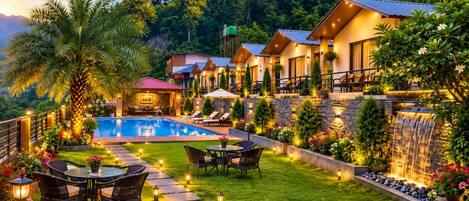 A well-lit outdoor area with a swimming pool, lounge chairs, and a waterfall feature.