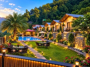 A well-lit outdoor area with a swimming pool, lounge chairs, and a waterfall feature. - The Aurum Resort (Mohan Chatti, Silogi Road)
