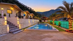 A pool area with a clear view of the pool, steps leading up to a building, and a mountain in the background. - The Aurum Resort (Mohan Chatti, Silogi Road)