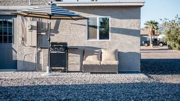 Une maison avec un barbecue, un canapé et un parasol.
