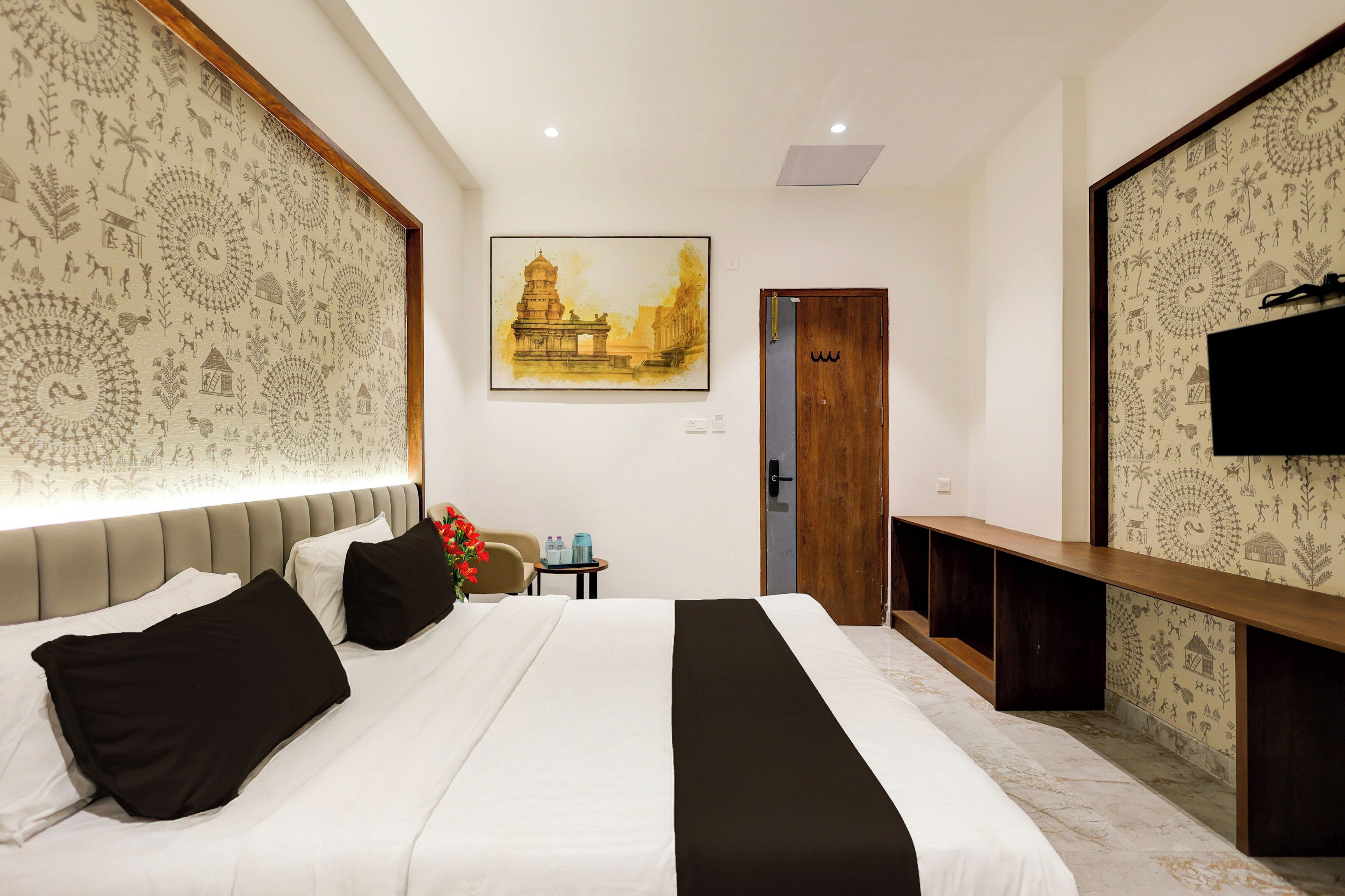 A hotel room with a bed, a painting of a temple, a TV, and patterned wallpaper.