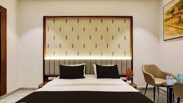 A hotel room with a large bed, a headboard with a patterned design, two bedside tables, a chair, and a painting on the wall.