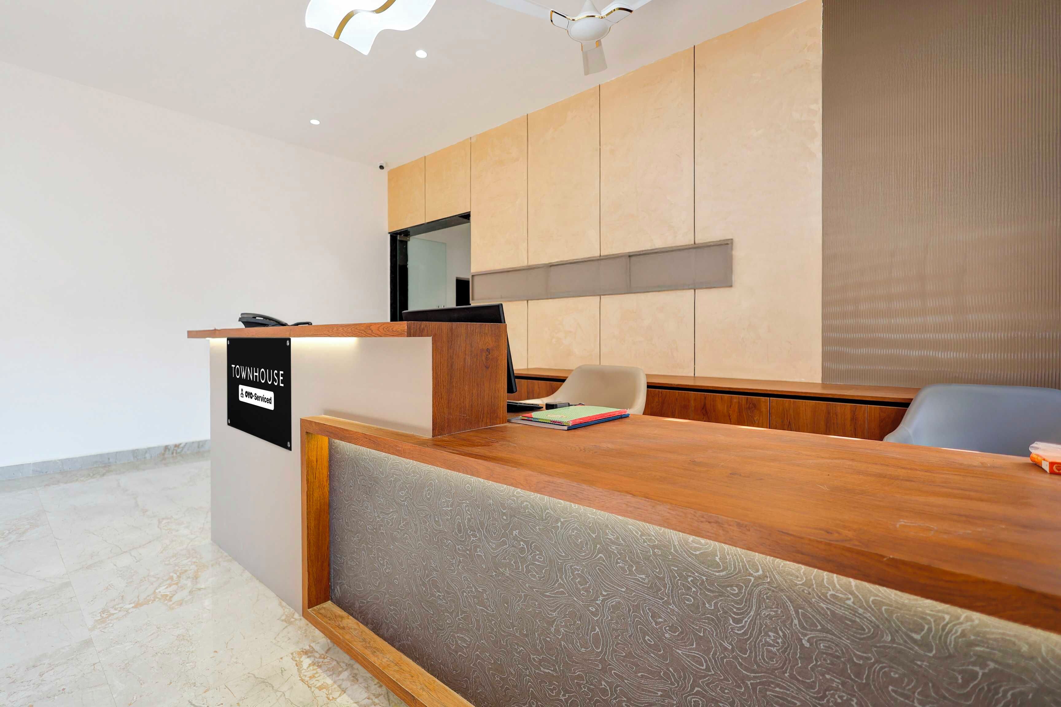 A reception desk with a wooden finish, a flat-screen TV mounted on the wall, and a seating area with a grey upholstered chair.