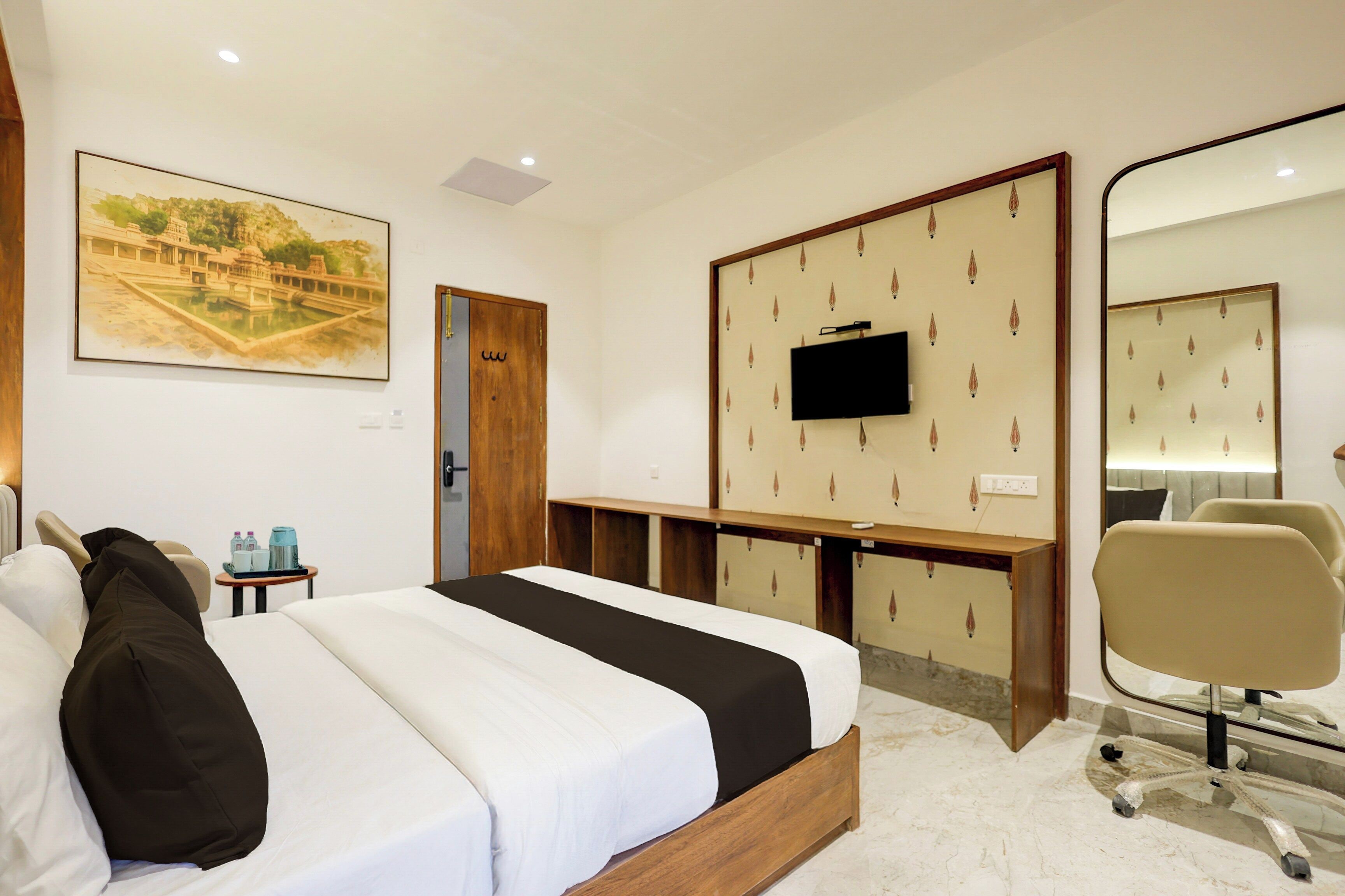 Ein Hotelzimmer mit einem Bett, einem Schreibtisch, einem Fernseher, einem Sessel und einem großen Spiegel.