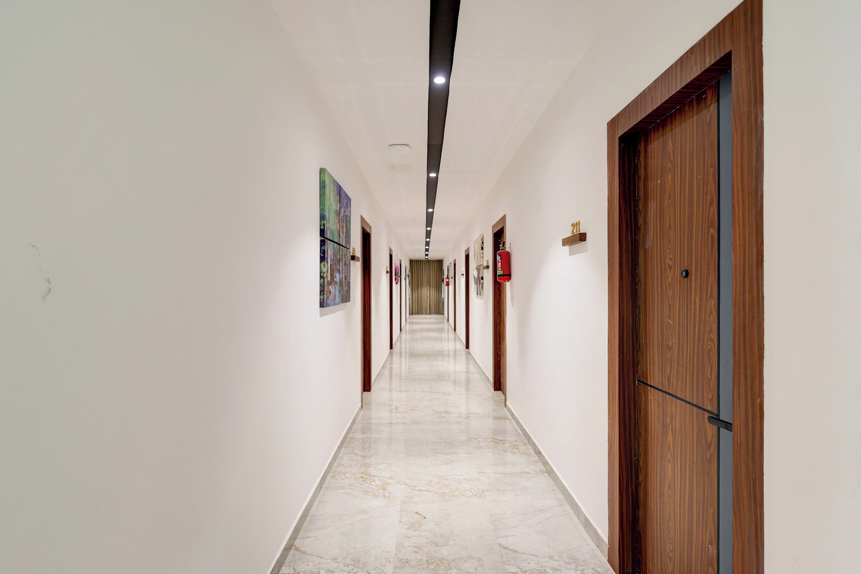 A long, narrow hallway with white walls and a marble floor. There are doors on both sides, and the hallway is well-lit with ceiling lights.