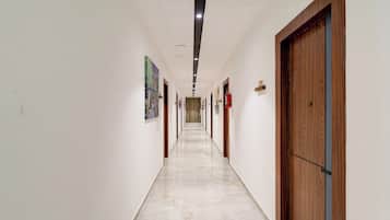 A long, narrow hallway with white walls and a marble floor. There are doors on both sides, and the hallway is well-lit with ceiling lights.
