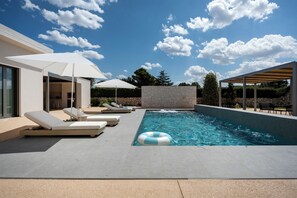 Un área de piscina moderna al aire libre con sillones reclinables y sombrillas.