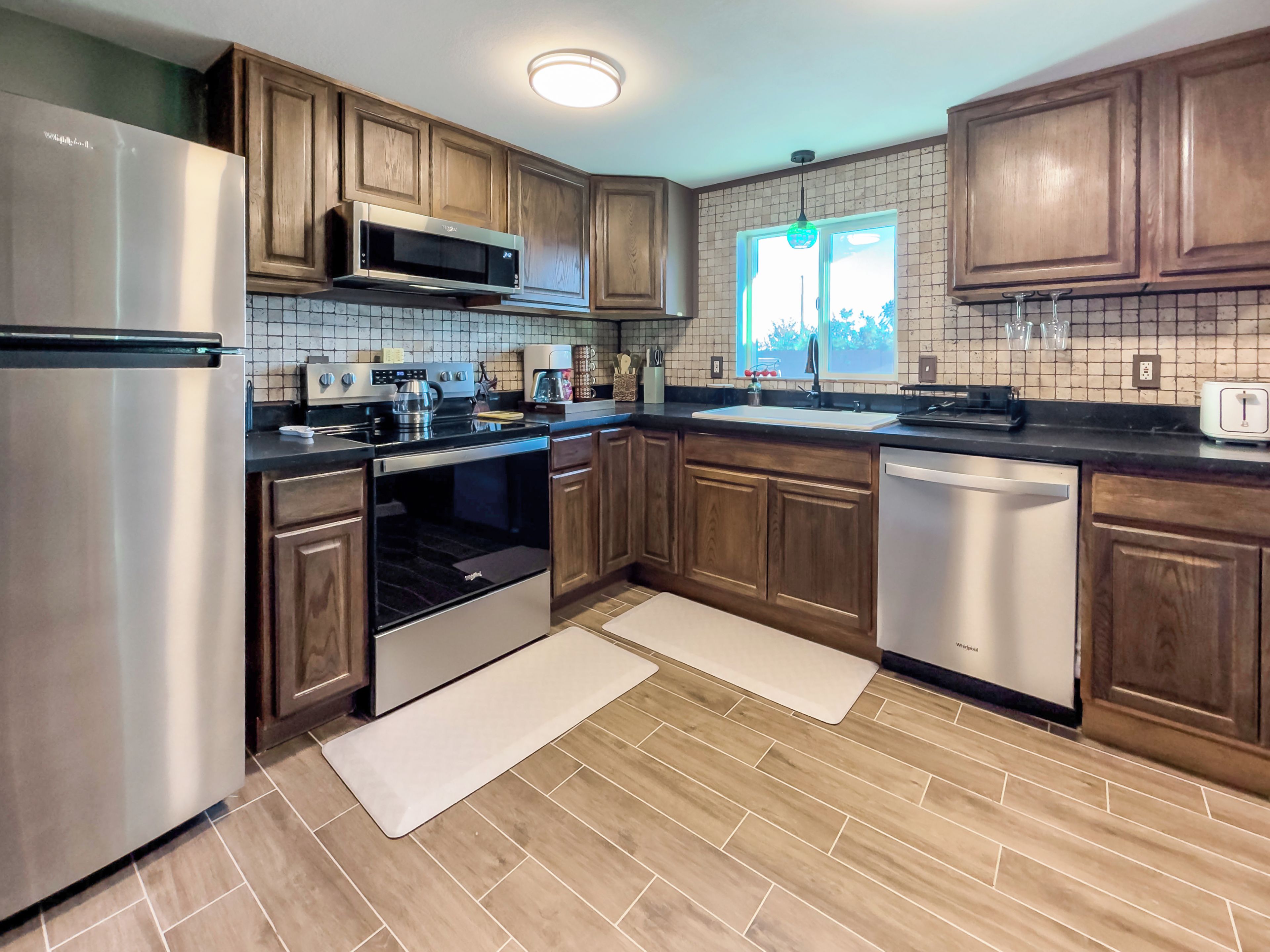 A modern kitchen with wooden cabinets, stainless steel appliances, a tiled backsplash, and a window with a view.