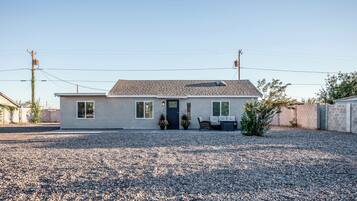 A single-story house with a gravel driveway, a front porch with seating, and a small garden.