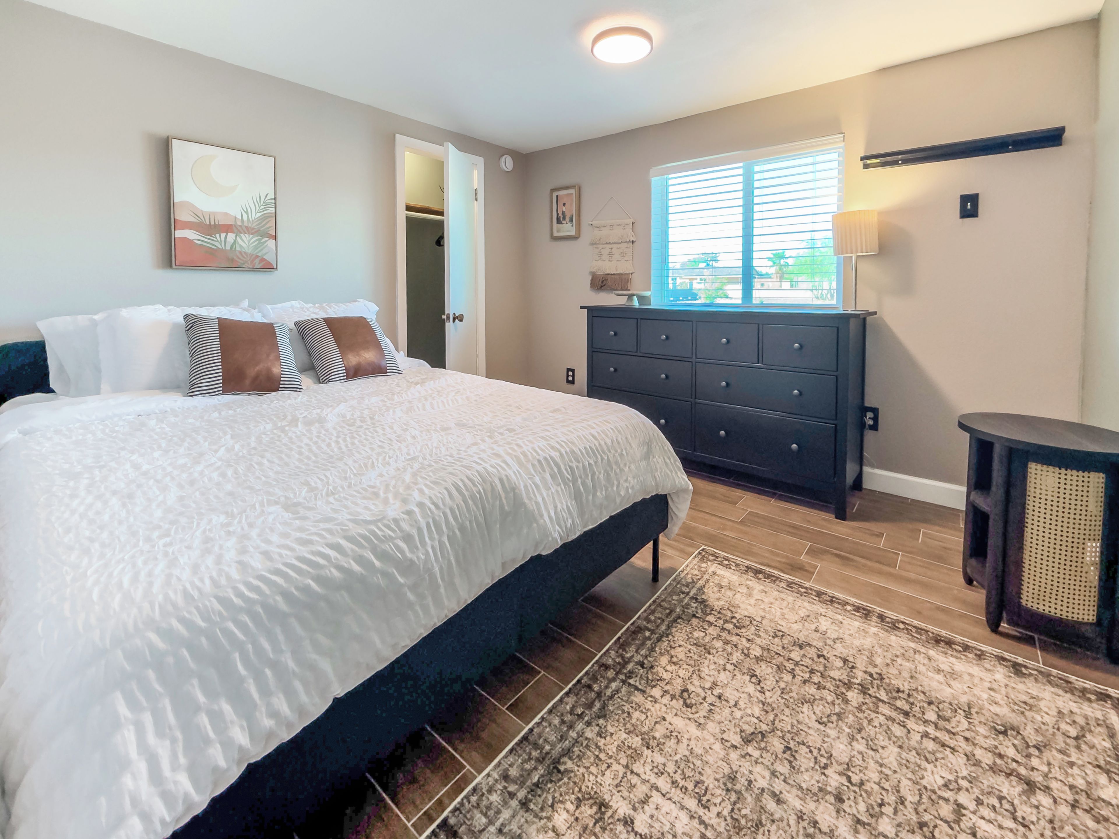 A bedroom with a bed, dresser, and a window with blinds.