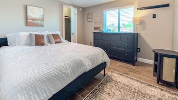 A bedroom with a bed, dresser, and a window with blinds.