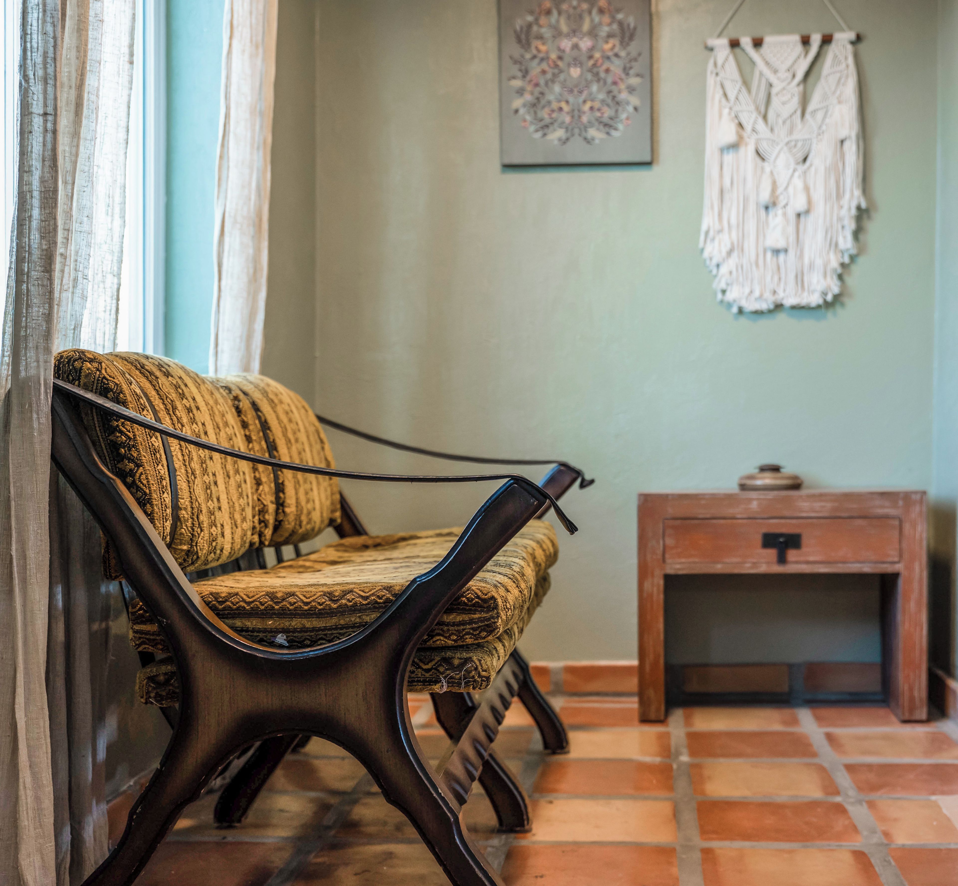 A room with a sofa, a small wooden table, and a macramé wall hanging.