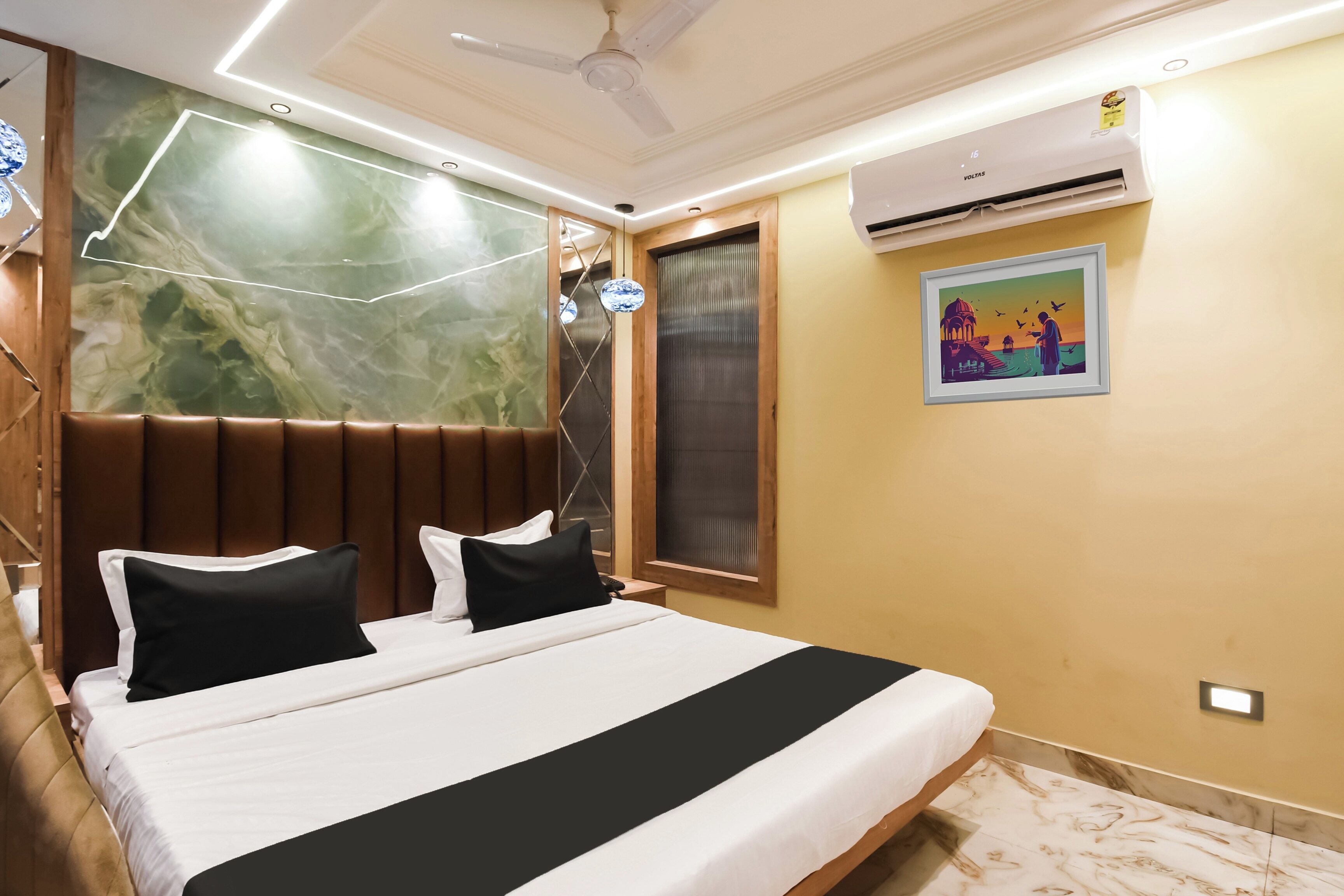 Una habitación de hotel con una cama, ventilador de techo, unidad de aire acondicionado y una obra de arte colgada en la pared.