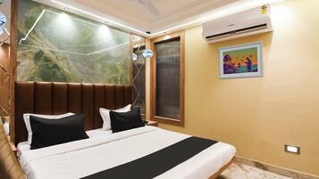 Una habitación de hotel con una cama, ventilador de techo, unidad de aire acondicionado y una obra de arte colgada en la pared.