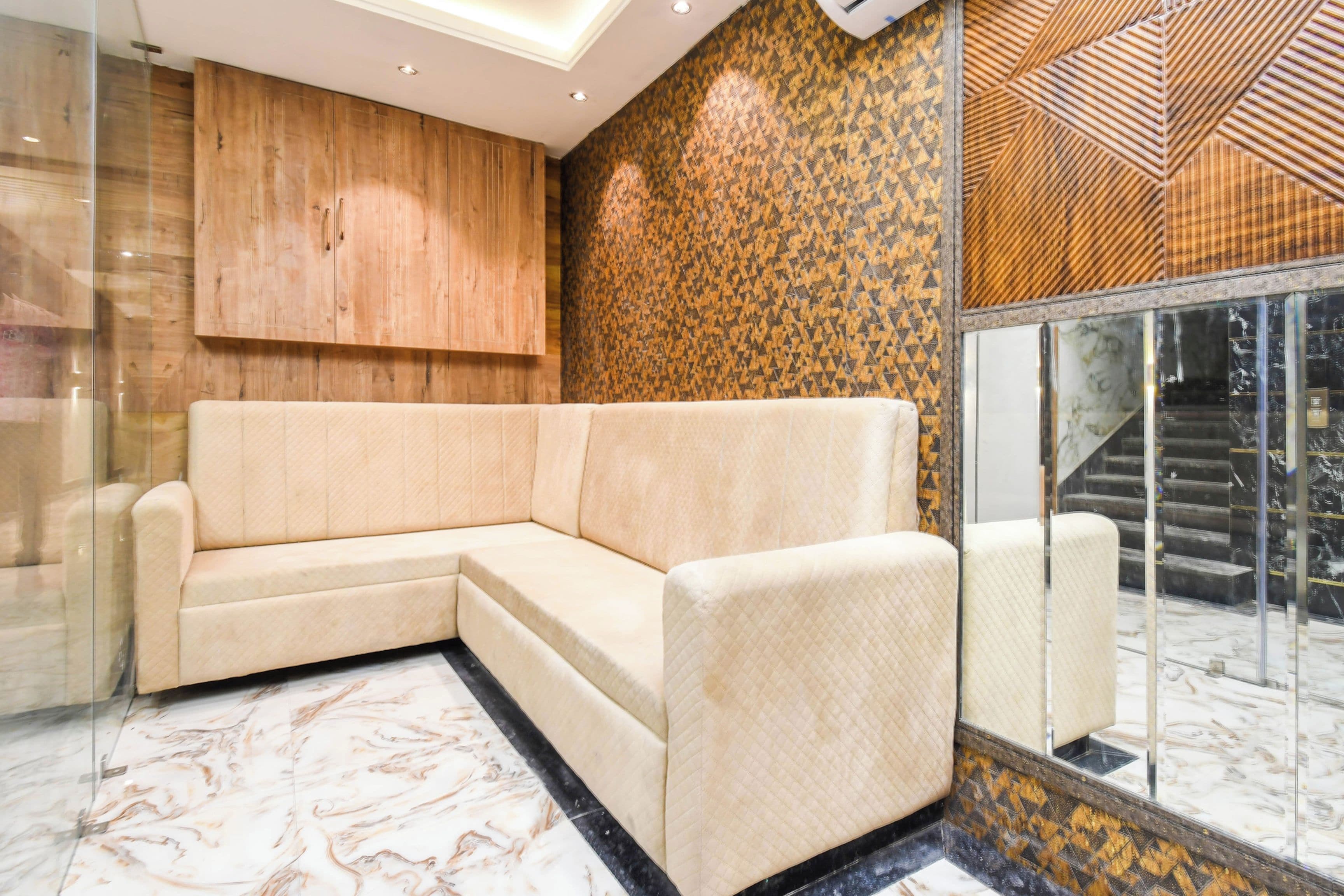 Un interior moderno con un sofá seccional color beige, un mueble de madera, pared con diseño y un vidrio que da a una escalera.