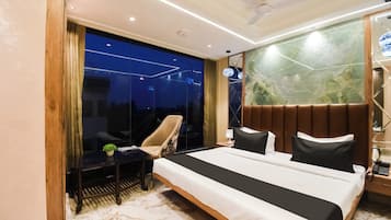 Habitación de hotel moderna con una cama grande, una zona de estar con una silla, una mesita y vistas a través de un muro de cristal.