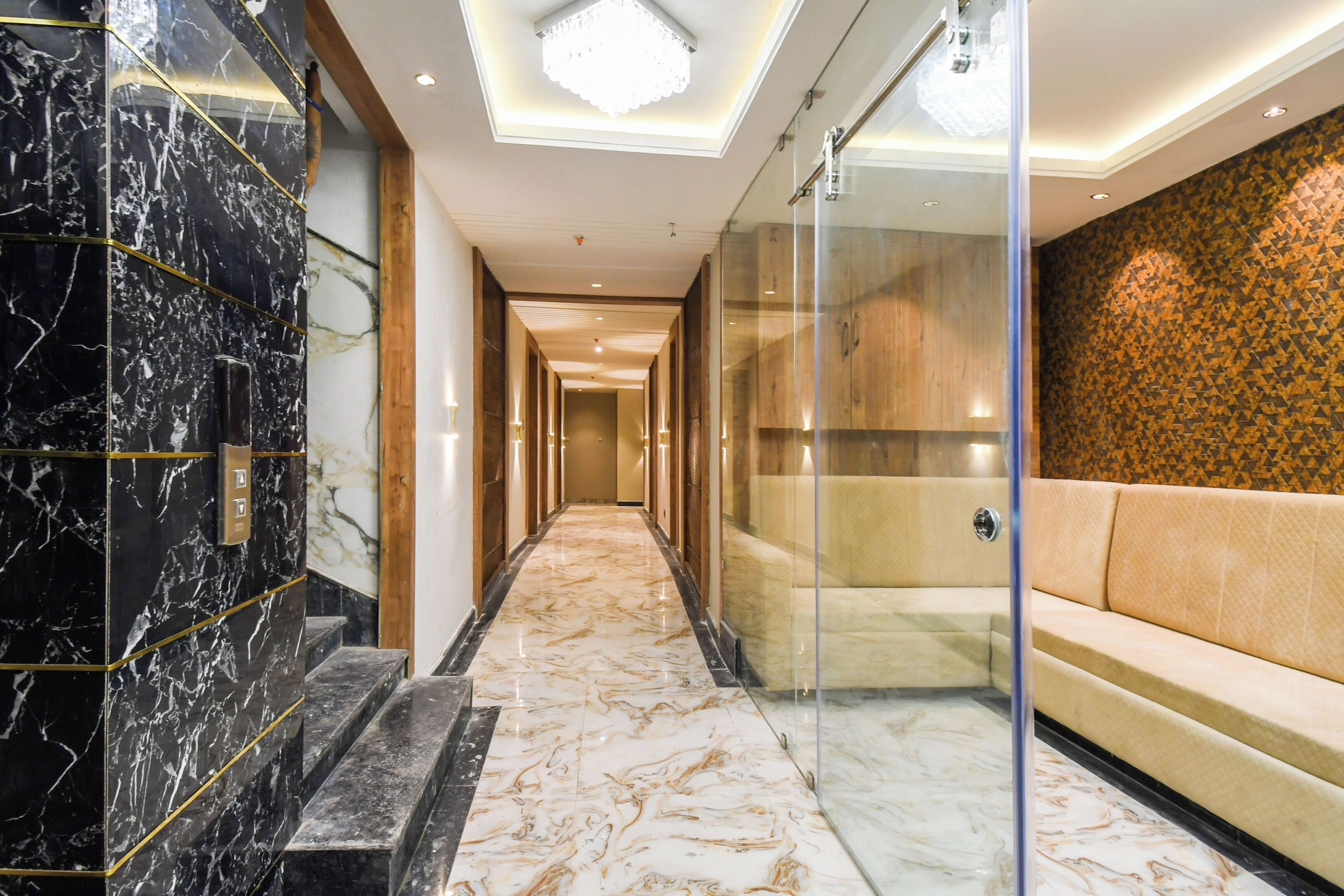 A hotel corridor with marble flooring, a glass wall, and a seating area with a patterned wall.