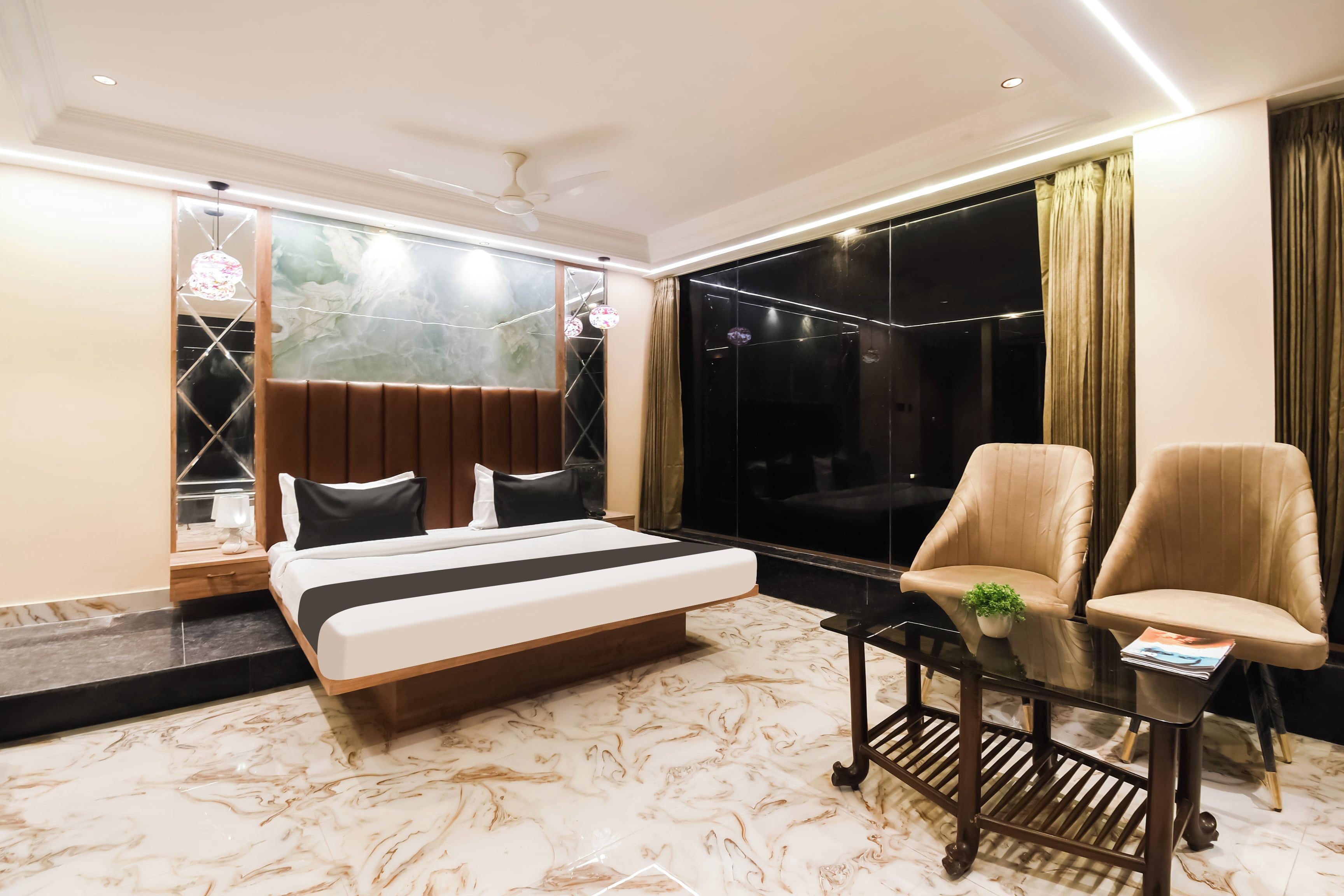 Habitación de hotel moderna con una cama grande, dos sillones, una mesita y un ventanal con cortinas.
