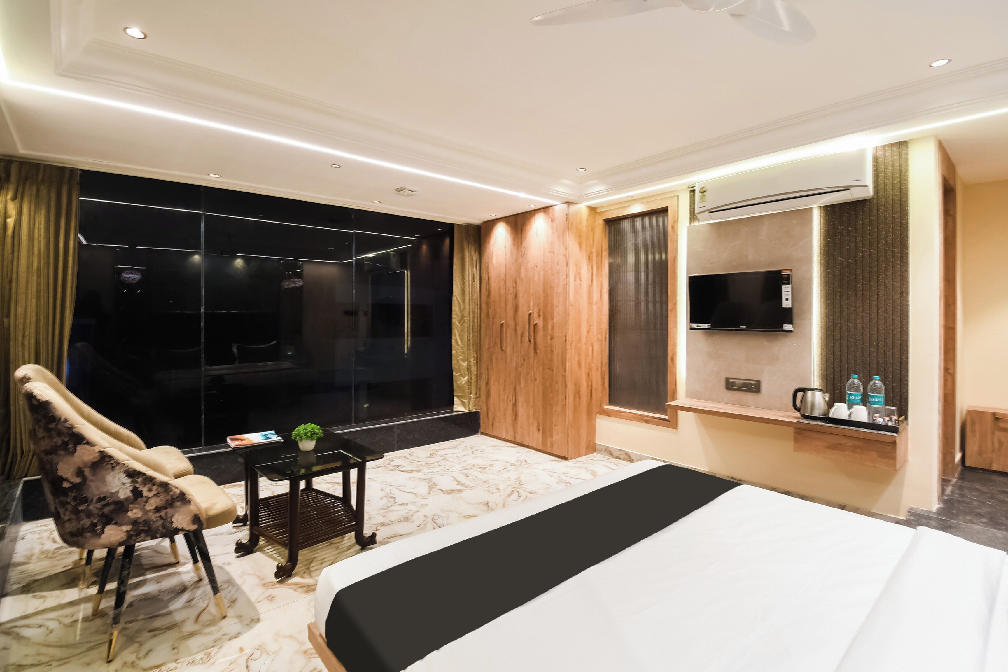 Habitación de hotel con una cama grande, una zona de estar con una silla, una mesita, televisión y minibar.