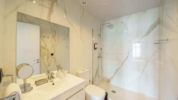 A modern bathroom with a marble vanity, a glass-enclosed shower, and a large mirror.