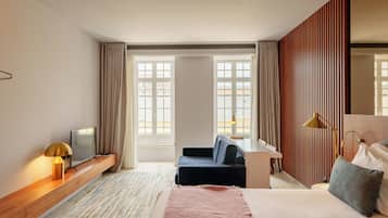 A modern hotel room with a bed, a desk, a sofa, a TV, and large windows.